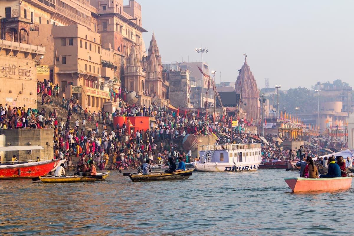 The ghats of Varanasi along the Ganges at dusk during Diwali — terraces of steps descending to the river, oil lamps, devotional fires and crowds.